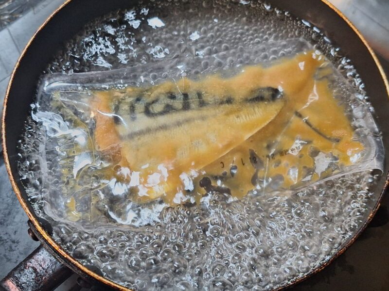 さばの味噌煮の真空パウチをフライパンで茹でる様子